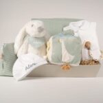 Canastilla bebé Dulces sueños compuesta por : Conejito de peluche BUNNY Peluche fabricado por Artesavi hecho a mano y confeccionado utilizando materiales de la más alta calidad, sus superficies son lavables. Este producto dispone de los ensayos de laboratorio y certificados según normativa Europea EN71-1 / EN71-2 / EN71-3 , estando exentos de tintes tóxicos y partes peligrosas garantizando así la total seguridad para los más pequeños. Medida : 32cm Personalizada la bandana con el nombre del bebé. Pelele manga larga aterciopelado, éste pijama además de estar diseñado especialmente para el descanso del bebé, mantiene la temperatura corporal del bebé al tiempo que se adapta perfectamente a su cuerpo lo que garantiza su comodidad durante el descanso. Composición : terciopelo 80% algodón y 20% polyester Gorrito bebé de algodón, personalizado mediante bordado. Cubo blandito de actividades de Little Dutch, este suave cubo de actividades contiene muchas actividades que estimulan los sentidos del bebé. Hay mucho por descubrir y jugar: varias etiquetas, diferentes texturas, un espejo y un sonajero que suena con cada movimiento. También hay una pequeña rana a la que le gusta jugar al escondite. Este juguete asegura momentos divertidos en el parque. Medidas : 15 x 15 x 15 cm Manta de piqué waffle algodón Manta ligera de piqué waffle y forro de coralina, ligera, calentita, fácil de plegar y limpiar. La coralina está fabricada con un innovador y renovado tejido polar, un moderno textil que le ofrece mejores propiedades térmicas. Se caracteriza por su tacto sedoso, textura muy suave, aspecto brillante, y mantener mejor el calor del bebé. Su tacto suave y agradable ofrece al bebé la opción de estar siempre junto a un peluche. Medidas aprox. : 70x100 cm Personalizable Precioso neceser bebé personalizable con la inicial o nombre del bebé donde podrás poner las cositas necesarias para su aseo, tanto si vas de paseo como de viaje. Neceser de piqué waffle