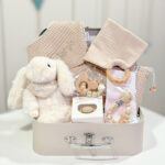 Canastilla bebé Bunny compuesta por peluche conejito con bandana personalizada con el nombre del bebé, chupetero de silicona modelo Momma personalizado, mordedor de silicona con figura de madera natural haya, chupete retro nordic personalizado, doudou muselina con aro de madera natural de haya personalizado, bandana de waffle algodón personalizado y neceser de waffle algodón personalizado. Todos los productos se presentan en una bonita y práctica maletita también personalizada con el nombre del bebé.