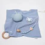 Pack regalo Hi Baby compuesto por Doudou muselina con aro de madera natural de haya, personalizado con el nombre del bebé. La muselina es una tela de algodón orgánico muy suave,manejable, cómoda, esponjosa, ligera y agradable al tacto, tambien se denomina gasa de algodón. Todas las telas que utilizamos para el doudou muselina están certificadas con el sello STANDARD 100 by OEKO-TEX® que garantiza la ausencia de sustancias nocivas en el producto, esencial para el contacto directo con la piel para bebes y niñ@s de hasta tres años. Doudou muselina de doble capa, las medidas son 40cm x 40cm. Será uno de sus juguetes favoritos a modo de doudou. Para los más pequeños es muy fácil cogerlo, agarrarlo con fuerza y manejarlo. Calmará al bebé cuando empiece con la dentición. También se puede sustituir el aro por el chupete, actuando como chupetero. Personalizado el aro de madera con el nombre del bebé, confección artesanal elaborado por Hi Baby! Este guardachupetes bebé de silicona es perfecto para conservar los chupetes limpios hasta su uso, evitar que se pierdan y lo mejor, tenerlos siempre a mano cuando se necesita, con esta funda para chupetes colocada en las asas del cochecito se podrá recuperar rápidamente el chupete de bebé sin tener que buscar en su bolsa. El portachupetes es un accesorio clave y sobretodo muy práctico en cada salida, siendo el lugar ideal para guardar y mantenerlo siempre alejado de gérmenes y bacterias. El portachupetes para bebé es un accesorio esencial para muchos padres, ya que permite llevar y almacenar los chupetes del bebé de manera higiénica y organizada, puede guardar hasta 2 chupetes, y así disponer de un segundo chupete de repuesto, su tamaño compacto permite guardarla en cualquier bolsillo, pero si lo cuelgas del carro, lo agradecerás. Su correa de silicona facilita el transporte y evita que se pierda, puede ser útil para colgar el portachupetes del cochecito, de la bolsa del pañal o la muñeca del adulto