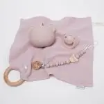 Pack regalo Hi Baby compuesto por Doudou muselina con aro de madera natural de haya, personalizado con el nombre del bebé. La muselina es una tela de algodón orgánico muy suave,manejable, cómoda, esponjosa, ligera y agradable al tacto, tambien se denomina gasa de algodón. Todas las telas que utilizamos para el doudou muselina están certificadas con el sello STANDARD 100 by OEKO-TEX® que garantiza la ausencia de sustancias nocivas en el producto, esencial para el contacto directo con la piel para bebes y niñ@s de hasta tres años. Doudou muselina de doble capa, las medidas son 40cm x 40cm. Será uno de sus juguetes favoritos a modo de doudou. Para los más pequeños es muy fácil cogerlo, agarrarlo con fuerza y manejarlo. Calmará al bebé cuando empiece con la dentición. También se puede sustituir el aro por el chupete, actuando como chupetero. Personalizado el aro de madera con el nombre del bebé, confección artesanal elaborado por Hi Baby! Este guardachupetes bebé de silicona es perfecto para conservar los chupetes limpios hasta su uso, evitar que se pierdan y lo mejor, tenerlos siempre a mano cuando se necesita, con esta funda para chupetes colocada en las asas del cochecito se podrá recuperar rápidamente el chupete de bebé sin tener que buscar en su bolsa. El portachupetes es un accesorio clave y sobretodo muy práctico en cada salida, siendo el lugar ideal para guardar y mantenerlo siempre alejado de gérmenes y bacterias. El portachupetes para bebé es un accesorio esencial para muchos padres, ya que permite llevar y almacenar los chupetes del bebé de manera higiénica y organizada, puede guardar hasta 2 chupetes, y así disponer de un segundo chupete de repuesto, su tamaño compacto permite guardarla en cualquier bolsillo, pero si lo cuelgas del carro, lo agradecerás. Su correa de silicona facilita el transporte y evita que se pierda, puede ser útil para colgar el portachupetes del cochecito, de la bolsa del pañal o la muñeca del adulto
