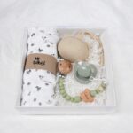 Pack regalo Hi Baby compuesto por Doudou muselina con aro de madera natural de haya, personalizado con el nombre del bebé. La muselina es una tela de algodón orgánico muy suave,manejable, cómoda, esponjosa, ligera y agradable al tacto, tambien se denomina gasa de algodón. Todas las telas que utilizamos para el doudou muselina están certificadas con el sello STANDARD 100 by OEKO-TEX® que garantiza la ausencia de sustancias nocivas en el producto, esencial para el contacto directo con la piel para bebes y niñ@s de hasta tres años. Doudou muselina de doble capa, las medidas son 40cm x 40cm. Será uno de sus juguetes favoritos a modo de doudou. Para los más pequeños es muy fácil cogerlo, agarrarlo con fuerza y manejarlo. Calmará al bebé cuando empiece con la dentición. También se puede sustituir el aro por el chupete, actuando como chupetero. Personalizado el aro de madera con el nombre del bebé, confección artesanal elaborado por Hi Baby! Este guardachupetes bebé de silicona es perfecto para conservar los chupetes limpios hasta su uso, evitar que se pierdan y lo mejor, tenerlos siempre a mano cuando se necesita, con esta funda para chupetes colocada en las asas del cochecito se podrá recuperar rápidamente el chupete de bebé sin tener que buscar en su bolsa. El portachupetes es un accesorio clave y sobretodo muy práctico en cada salida, siendo el lugar ideal para guardar y mantenerlo siempre alejado de gérmenes y bacterias. El portachupetes para bebé es un accesorio esencial para muchos padres, ya que permite llevar y almacenar los chupetes del bebé de manera higiénica y organizada, puede guardar hasta 2 chupetes, y así disponer de un segundo chupete de repuesto, su tamaño compacto permite guardarla en cualquier bolsillo, pero si lo cuelgas del carro, lo agradecerás. Su correa de silicona facilita el transporte y evita que se pierda, puede ser útil para colgar el portachupetes del cochecito, de la bolsa del pañal o la muñeca del adult