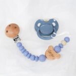 Pack regalo Hi Baby compuesto por Doudou muselina con aro de madera natural de haya, personalizado con el nombre del bebé. La muselina es una tela de algodón orgánico muy suave,manejable, cómoda, esponjosa, ligera y agradable al tacto, tambien se denomina gasa de algodón. Todas las telas que utilizamos para el doudou muselina están certificadas con el sello STANDARD 100 by OEKO-TEX® que garantiza la ausencia de sustancias nocivas en el producto, esencial para el contacto directo con la piel para bebes y niñ@s de hasta tres años. Doudou muselina de doble capa, las medidas son 40cm x 40cm. Será uno de sus juguetes favoritos a modo de doudou. Para los más pequeños es muy fácil cogerlo, agarrarlo con fuerza y manejarlo. Calmará al bebé cuando empiece con la dentición. También se puede sustituir el aro por el chupete, actuando como chupetero. Personalizado el aro de madera con el nombre del bebé, confección artesanal elaborado por Hi Baby! Este guardachupetes bebé de silicona es perfecto para conservar los chupetes limpios hasta su uso, evitar que se pierdan y lo mejor, tenerlos siempre a mano cuando se necesita, con esta funda para chupetes colocada en las asas del cochecito se podrá recuperar rápidamente el chupete de bebé sin tener que buscar en su bolsa. El portachupetes es un accesorio clave y sobretodo muy práctico en cada salida, siendo el lugar ideal para guardar y mantenerlo siempre alejado de gérmenes y bacterias. El portachupetes para bebé es un accesorio esencial para muchos padres, ya que permite llevar y almacenar los chupetes del bebé de manera higiénica y organizada, puede guardar hasta 2 chupetes, y así disponer de un segundo chupete de repuesto, su tamaño compacto permite guardarla en cualquier bolsillo, pero si lo cuelgas del carro, lo agradecerás. Su correa de silicona facilita el transporte y evita que se pierda, puede ser útil para colgar el portachupetes del cochecito, de la bolsa del pañal o la muñeca del adult