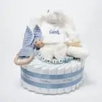 Tarta de pañales 1 piso LITTLE BUNNY compuesto por 28 unidades marca Dodot Sensitive T2, peluche principal conejito personalizado, mordedor de piqué waffle de algodón y aro de madera personalizado, sujeta chupetes de silicona modelo Momma personalizado y juego calcetines bebé de algodón. Dimensiones altura 35cm x 22cm ancho.