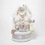 Tarta de pañales de dos pisos compuesta por 44 unidades marca Dodot sensitive, peluche principal conejito con bandana personalizada , mordedor orejitas de piqué waffle, algodón y madera personalizado, sujeta chupetes de silicona personalizado, cepillo y peine para bebé de madera 100% natural personalizados, bandana de piqué waffle y algodón, mordedor de silicona y madera, dou dou animalito. Dimensiones altura 45cm x 26cm ancho.