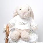 Tarta de pañales de dos pisos compuesta por 44 unidades marca Dodot Sensitive T2, peluche principal conejito personalizado, conjunto cepillo y peine bebé de madera personalizado, sujeta chupetes de silicona personalizado y juego calcetines bebé. Dimensiones altura 45cm x 26cm ancho. Color Beige/Toffe