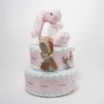 Tarta de pañales de dos pisos compuesta por 44 unidades marca Dodot Sensitive T2, peluche principal conejito personalizado, conjunto cepillo y peine bebé de madera personalizado con el nombre del bebé, sujeta chupetes de silicona personalizado con el nombre del bebé y juego calcetines bebé. Dimensiones altura 45cm x 26cm ancho. Color Rosa bebé