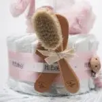 Tarta de pañales de dos pisos compuesta por 44 unidades marca Dodot Sensitive T2, peluche principal conejito personalizado, conjunto cepillo y peine bebé de madera personalizado con el nombre del bebé, sujeta chupetes de silicona personalizado con el nombre del bebé y juego calcetines bebé. Dimensiones altura 45cm x 26cm ancho. Color Rosa bebé