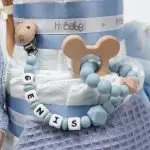 Tarta de pañales 3 pisos SPECIAL CAKE compuesto por 52 unidades marca Dodot sensitive, peluche principal conejito personalizado, sujeta chupetes de silicona Momma, mordedor orejitas piqué waffle algodón con aro de madera personalizado con el nombre del bebé, cepillo y peine para bebé de madera 100% natural personalizado con el nombre del bebé, mordedor de silicona Momma, bandana de piqué waffle y Doudou animalito personalizado con el nombre del bebé. Dimensiones altura 55cm x 26cm ancho. Color Azul Jean.