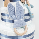Mordedor orejero waffle en Tarta de pañales 3 pisos Sweet Cake compuesto por 52 unidades marca Dodot, peluche principal conejito personalizado, sujeta chupetes de silicona, mordedor orejitas piqué waffle,algodón y madera, cepillo para bebé de madera 100% natural, mordedor de silicona y bandana de piqué waffle. Dimensiones altura 55cm x 26cm ancho. Color azul jean