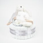 Tarta de pañales 1 piso LITTLE BUNNY compuesto por 28 unidades marca Dodot Sensitive T2, peluche principal conejito personalizado, mordedor de piqué waffle de algodón y aro de madera personalizado, sujeta chupetes de silicona modelo Momma personalizado y juego calcetines bebé de algodón. Dimensiones altura 35cm x 22cm ancho. Color Gris