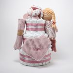 Tarta de pañales de 3 pisos compuesto por 52 unidades marca Dodot sensitive, pelota sensorial Montessori de Little Dutch, mordedor orejitas de tela piqué waffle algodón y aro de madera natural personalizado con el nombre del bebé, bandana de tela piqué waffle algodón personalizable, chupetero de silicona y crochet con pinza de madera natural de haya, paño de lactancia de piqué waffle algodón, muñeca ANNA de Little Dutch 35cm. Stick de madera personalizado con el nombre del bebé. Dimensiones altura 42cm x 27cm ancho. Color Rosa palo