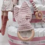 Tarta de pañales de 3 pisos compuesto por 52 unidades marca Dodot sensitive, pelota sensorial Montessori de Little Dutch, mordedor orejitas de tela piqué waffle algodón y aro de madera natural personalizado con el nombre del bebé, bandana de tela piqué waffle algodón personalizable, chupetero de silicona y crochet con pinza de madera natural de haya, paño de lactancia de piqué waffle algodón, muñeca ANNA de Little Dutch 35cm. Stick de madera personalizado con el nombre del bebé. Dimensiones altura 42cm x 27cm ancho. Color Rosa palo