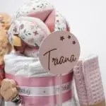 Tarta de pañales de 3 pisos compuesto por 52 unidades marca Dodot sensitive, pelota sensorial Montessori de Little Dutch, mordedor orejitas de tela piqué waffle algodón y aro de madera natural personalizado con el nombre del bebé, bandana de tela piqué waffle algodón personalizable, chupetero de silicona y crochet con pinza de madera natural de haya, paño de lactancia de piqué waffle algodón, muñeca ANNA de Little Dutch 35cm. Stick de madera personalizado con el nombre del bebé. Dimensiones altura 42cm x 27cm ancho. Color Rosa palo