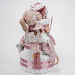 Tarta de pañales de 3 pisos compuesto por 52 unidades marca Dodot sensitive, pelota sensorial Montessori de Little Dutch, mordedor orejitas de tela piqué waffle algodón y aro de madera natural personalizado con el nombre del bebé, bandana de tela piqué waffle algodón personalizable, chupetero de silicona y crochet con pinza de madera natural de haya, paño de lactancia de piqué waffle algodón, muñeca ANNA de Little Dutch 35cm. Stick de madera personalizado con el nombre del bebé. Dimensiones altura 42cm x 27cm ancho. Color Rosa palo