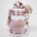 Tarta de pañales de 3 pisos compuesto por 52 unidades marca Dodot sensitive, pelota sensorial Montessori de Little Dutch, mordedor orejitas de tela piqué waffle algodón y aro de madera natural personalizado con el nombre del bebé, bandana de tela piqué waffle algodón personalizable, chupetero de silicona y crochet con pinza de madera natural de haya, paño de lactancia de piqué waffle algodón, muñeca ANNA de Little Dutch 35cm. Stick de madera personalizado con el nombre del bebé. Dimensiones altura 42cm x 27cm ancho. Color Rosa palo