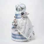Tarta de pañales de 3 pisos JIMMY compuesto por 52 unidades marca Dodot sensitive, pelota sensorial Montessori de Little Dutch, chupetero de silicona, mordedor de silicona con figura de madera natural de haya, muñeco JIMMY de Little Dutch 35cm., Chupetero muselina buho de Little Dutch, Doudou Sailors bay de Little Dutch, stick de madera personalizado con el nombre del bebé. Dimensiones altura 42cm x 27cm ancho. Color Azul jean