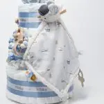 Tarta de pañales de 3 pisos JIMMY compuesto por 52 unidades marca Dodot sensitive, pelota sensorial Montessori de Little Dutch, chupetero de silicona, mordedor de silicona con figura de madera natural de haya, muñeco JIMMY de Little Dutch 35cm., Chupetero muselina buho de Little Dutch, Doudou Sailors bay de Little Dutch, stick de madera personalizado con el nombre del bebé. Dimensiones altura 42cm x 27cm ancho. Color Azul jean