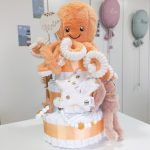 Tarta de pañales de tres pisos pulpito compuesto por 52 unidades marca Dodot sensitive, peluche principal Pulpo dorado 40cm, increiblemente suave y decorativo, chupetero de silicona con pinza de silicona de grado alimentario libre de BPA, PVC, Ftalatos, cadmio y plomo, mordedor de silicona con figura de madera natural haya, bandana secababitas de piqué waffle, chupetero de tela estrella de Little Dutch 15cm x 15cm, cepillo y peine personalizados con el nombre del bebé de madera natural, sonajero conejo orejitas de Artesavi 35cm, stick de madera personalizado con el nombre del bebé. Dimensiones altura 45cm x 26cm ancho. Color Melocotón