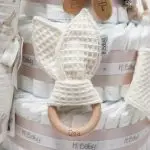 Tarta pañales V. Sunny Champagne compuesto por 84 unidades marca Dodot, peluche principal Mocca de Teddykompaniet 25 cm, chupetero de silicona de grado alimentario libre de BPA, PVC, Ftalatos, cadmio y plomo, bandana secababitas, chupete personalizado, mordedor orejitas y capa de baño de piqué waffle personalizada de Hi Baby, Doudou baby bunny personalizado, conjunto de cepillo y peine de madera personalizado hecho con materiales 100% naturales de lana de cabra y madera de haya, ofreciendo una experiencia cómoda y suave para tu bebé. Ideal para el cuero cabelludo sensible de los más pequeños, guardachupetes de silicona perfecto para guardar el chupete cuando no se está usando, body de babidu personalizado con el dibujo de un conejito y el nombre del bebé. Dimensiones altura 56cm x 30cm ancho. Color Champagne
