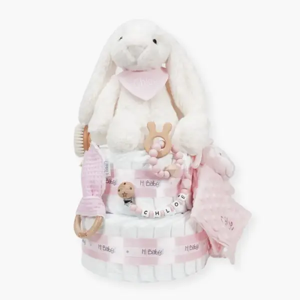 Tarta de pañales de dos pisos compuesta por 44 unidades marca Dodot sensitive, peluche principal conejito con bandana personalizada , mordedor orejitas de piqué waffle, algodón y madera personalizado, sujeta chupetes de silicona personalizado, cepillo y peine para bebé de madera 100% natural personalizados, bandana de piqué waffle y algodón, mordedor de silicona y madera, dou dou animalito. Dimensiones altura 45cm x 26cm ancho.