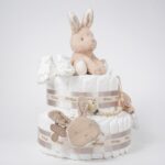 Tarta de pañales Baby Bunny 2 pisos compuesto por 44 unidades marca Dodot sensitive T2, peluche principal conejito colección Baby Bunny, Botitas patucos con estampado colección Baby Bunny, fabricados con algodón 100% orgánico. Chupetero de silicona con pinza de silicona de alta calidad, personalizado con el nombre del bebé, elaborado por Hi Baby , Sonajero anillo conejito de la colección baby bunny, de Little Dutch. Chupetero de tela muselina, colección baby bunny. Dimensiones altura 38cm x 28cm ancho. Color Beige/Toffe