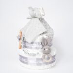 Tarta de pañales de dos pisos compuesta por 44 unidades marca Dodot, peluche principal Doudou personalizable, mordedor orejitas de crochet y madera personalizado, sujeta chupetes de silicona personalizado, conjunto de cepillo y peine bebé personalizados. Dimensiones altura 40cm x 26cm ancho. Color Gris