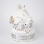 Tarta de pañales de dos pisos compuesta por 44 unidades marca Dodot, peluche principal Doudou personalizable, mordedor orejitas de crochet y madera, sujeta chupetes de silicona personalizado, conjunto de cepillo y peine bebé de madera personalizados. Dimensiones altura 40cm x 26cm ancho. Color Beige