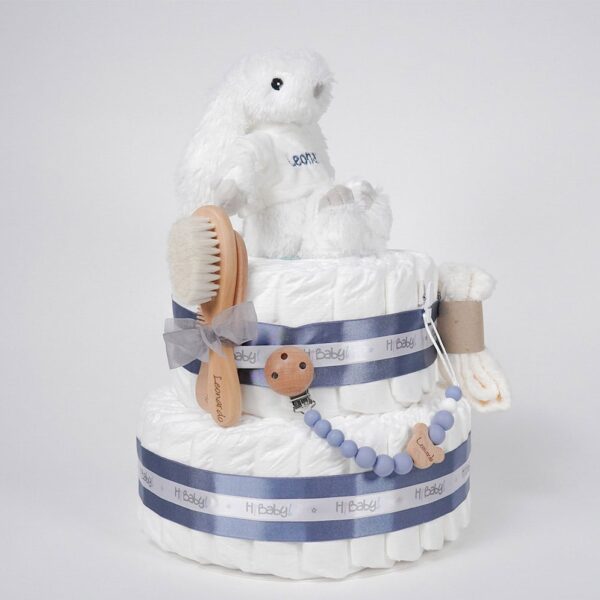 Tarta de pañales 2 pisos Beau Bebé, tarta de dos pisos compuesta por 44 unidades marca Dodot, peluche principal conejito personalizado, conjunto cepillo y peine bebé de madera personalizado, sujeta chupetes de silicona personalizado y juego calcetines bebé. Dimensiones altura 45cm x 26cm ancho. Color Azul oscuro