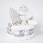 Tarta de pañales de un piso compuesto por 20 unidades marca Dodot Sensitive T2, peluche principal conejito personalizado, mordedor de piqué waffle de algodón y aro de madera personalizado, sujeta chupetes de silicona modelo Momma personalizado y juego calcetines bebé de algodón. Dimensiones altura 35cm x 22cm ancho. Color Gris