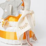 Tarta de pañales de tres pisos compuesto por 52 unidades marca Dodot Sensitive, peluche principal pequeña oca de 18cm de altura está hecha de una felpa increiblemente suave ideal para el bebé, chupetero de silicona con pinza de silicona de grado alimentario libre de BPA, PVC, Ftalatos, cadmio y plomo, mordedor de silicona con figura de madera natural haya, paño lactancia de piqué waffle 35cm x 25cm, juguete con sonido oca de Little Dutch gran entretenimiento para el bebé con su sonido y alas crujientes hecha con felpa increiblemente suave 15cm de altura, Doudou ganso, 100% gasa de algodón doble, muselina muy suave aportando comodidad al bebé cuando duerme, dispone de varios añadidos para tocar y sentir, estimulando los sentidos del bebé, los nudos y patas son perfectos para acurrucarse o masticar cuando empiezan a salir los dientes puede actuar como chupetero dispone de enganche para chupete, medidas 43cm x 40cm., contando la cabeza y las patas, personalizado con el nombre del bebé, Chupetero de tela algodón pequeños gansos de Hi Baby! 18cm x 18cm. Dimensiones altura 50cm x 26cm ancho. Color Calabaza