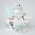 Tarta de pañales de un piso compuesto por 20 unidades marca Dodot Sensitive T2, peluche principal conejito personalizado, mordedor de piqué waffle de algodón y aro de madera personalizado, sujeta chupetes de silicona modelo Momma personalizado y juego calcetines bebé de algodón. Dimensiones altura 35cm x 22cm ancho. Color Verde Menta