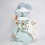 Tarta de pañales de tres pisos compuesto por 52 unidades marca Dodot sensitive, peluche principal conejito personalizado, sujeta chupetes de silicona, mordedor orejitas piqué waffle algodón y madera personalizado, cepillo y peine para bebé de madera 100% natural personalizado, mordedor de silicona, bandana de piqué waffle y Dou Dou personalizado. Dimensiones altura 55cm x 26cm ancho. Color Verde