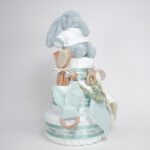 Tarta de pañales de tres pisos compuesto por 52 unidades marca Dodot sensitive, peluche principal conejito personalizado, sujeta chupetes de silicona, mordedor orejitas piqué waffle algodón y madera personalizado, cepillo y peine para bebé de madera 100% natural personalizado, mordedor de silicona, bandana de piqué waffle y Dou Dou personalizado. Dimensiones altura 55cm x 26cm ancho. Color Verde