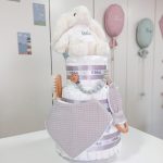 Tarta de pañales Sweet Cake de tres pisos compuesto por 52 unidades marca Dodot sensitive T2, peluche principal conejito personalizado, sujeta chupetes de silicona personalizable, mordedor orejitas piqué waffle algodón y madera personalizado, cepillo y peine para bebé de madera 100% natural personalizados, mordedor de silicona y bandana de piqué waffle personalizable. Dimensiones altura 55cm x 26cm ancho. Color Gris