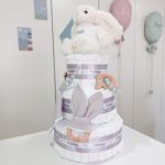 Tarta de pañales Sweet Cake de tres pisos compuesto por 52 unidades marca Dodot sensitive T2, peluche principal conejito personalizado, sujeta chupetes de silicona personalizable, mordedor orejitas piqué waffle algodón y madera personalizado, cepillo y peine para bebé de madera 100% natural personalizados, mordedor de silicona y bandana de piqué waffle personalizable. Dimensiones altura 55cm x 26cm ancho. Color Gris