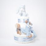 Tarta de pañales Sweet Cake de tres pisos compuesto por 52 unidades marca Dodot sensitive T2, peluche principal conejito personalizado, sujeta chupetes de silicona personalizable, mordedor orejitas piqué waffle algodón y madera personalizado, cepillo para bebé de madera 100% natural personalizado, mordedor de silicona y bandana de piqué waffle personalizable. Dimensiones altura 55cm x 26cm ancho. Color Azul