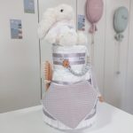 Tarta de pañales Sweet Cake de tres pisos compuesto por 52 unidades marca Dodot sensitive T2, peluche principal conejito personalizado, sujeta chupetes de silicona personalizable, mordedor orejitas piqué waffle algodón y madera personalizado, cepillo y peine para bebé de madera 100% natural personalizados, mordedor de silicona y bandana de piqué waffle personalizable. Dimensiones altura 55cm x 26cm ancho. Color Gris