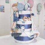 Tarta de pañales de 3 pisos compuesto por 52 unidades marca Dodot sensitive, pelota sensorial Montessori de Little Dutch, chupetero de silicona con pinza de silicona, mordedor de silicona con figura de madera natural de haya, muñeco JIMMY de Little Dutch 35cm., Chupetero de tela Sailors bay de Little Dutch, Doudou Sailors bay de Little Dutch, stick de madera personalizado con el mnombre del bebé. Dimensiones altura 42cm x 27cm ancho. Color Azul jean