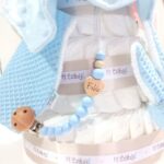 Tarta de pañales para gemelos o mellizos de 3 pisos, es el regalo perfecto para dar la bienvenida a los bebés recién nacidos. Contenido de la tarta de pañales para gemelos 3 pisos : 72 unidades pañales Dodot sensitive T2 alta absorción. Dos Dou Dou a conjunto con el color elegido, personalizados. Dos Sujetachupetes de silicona personalizados. Dos Mordedores orejitas de waffle, Dos bandanas secababitas de algodón waffle. Tarjeta de felicitación personalizada con el nombre de los bebés, dónde podrás expresar tú mensaje de bienvenida. Envuelto en papel de celofán transparente con lazo realizado en cinta especial Hi Baby. Caja de cartón con protección para el transporte. Dimensiones y color de la tarta de pañales para gemelos de 3 pisos: Altura 38cm. Ancho:26cm. Color: rosa, azul, gris, beige o toffee. Especificaciones de los productos que se incluyen en esta tarta de pañales para gemelos recién nacido: 3 pisos compuesto por 72 pañales Dodot® Sensitive T2 de alta absorción y protección con capa dermo confort, por lo que no irritan la piel delicada del bebé.Dos Dou Dou 28cm x 28cm confeccionado utilizando únicamente materiales de máxima calidad certificado según normativa Europea garantizando la total seguridad para los pequeños. Dos Mordedores orejitas de waffle y madera. Dos Sujetachupetes de silicona personalizados, Dos bandanas secababitas de algodón waffle, Todas nuestras telas están certificadas con el sello  STANDARD 100 by OEKO-TEX® que garantiza la ausencia de sustancias nocivas en el producto, apto para articulos que puedan estar en contacto directo con la piel para bebes y niñ@s de hasta tres años. El algodón waffle es una tela muy suave,manejable y cómoda, tremendamente esponjosa adquiere su nombre por los cuadraditos en relieve, que hacen la forma de un gofre o bien de un nido de abeja. Medidas.- 29cm x 15cm Realizado a mano con cierre de velcro muy cómodo para su ajuste. Personalizable con el nombre de los bebés.